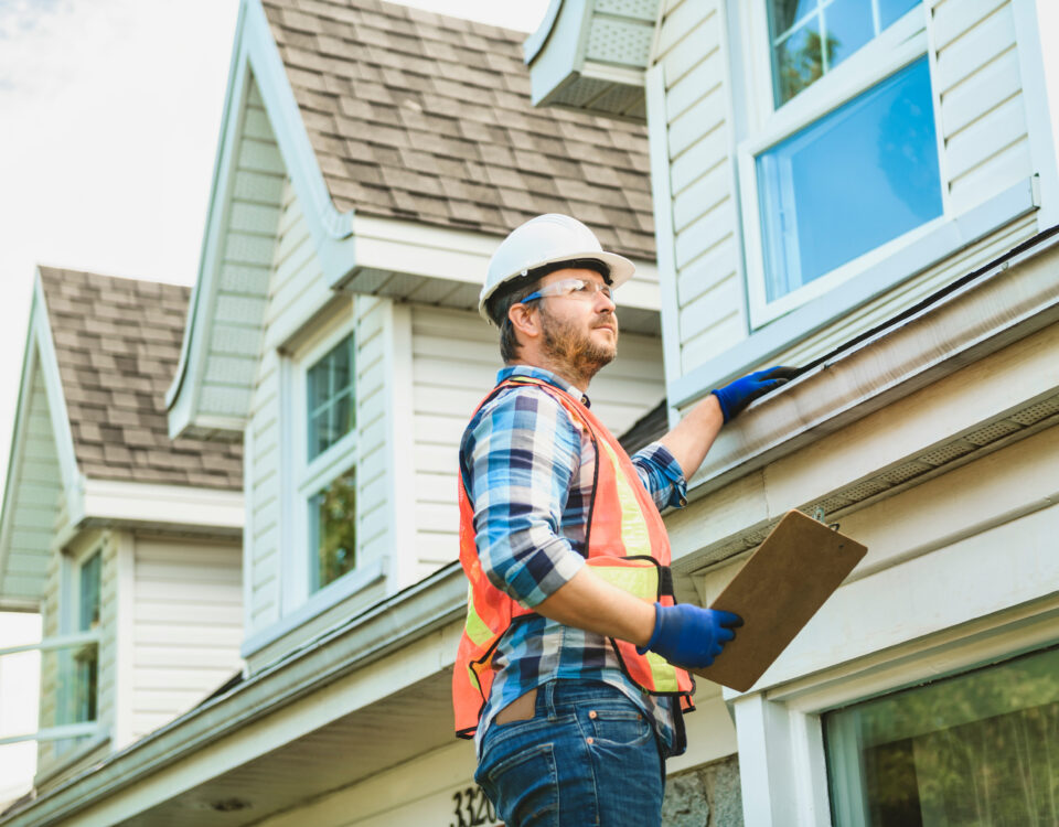 man with hard hat standing on steps inspecting house roof